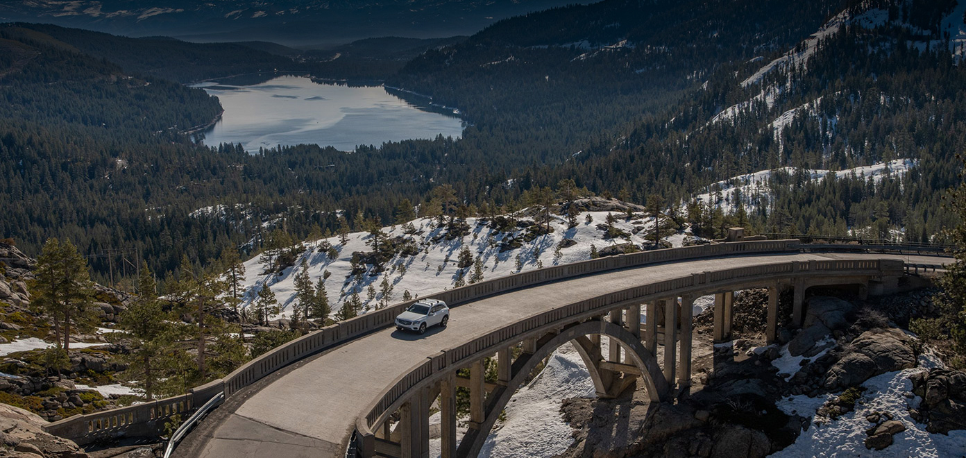 White car driving across bridge, snow and trees in the background | Quality Automotive Servicing